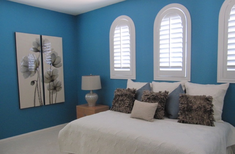 White arched plantation shutters in blue bedroom